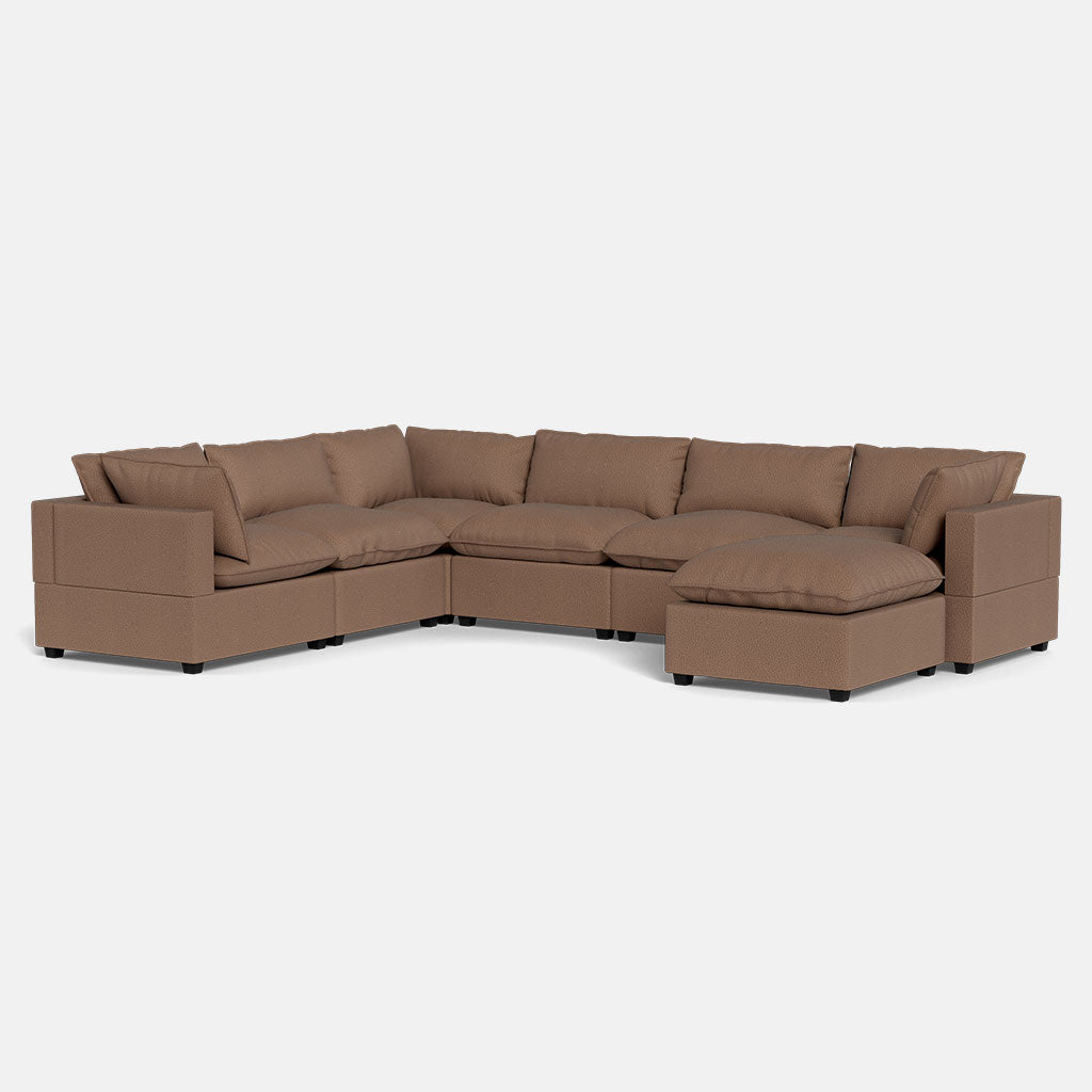 The Kova Pillow Cushion Grand Corner + Ottoman is a spacious, L-shaped sectional sofa with brown upholstery, plush cushions, and a right-side chaise lounge, shown against a plain white background.