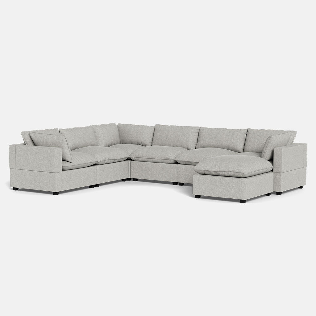 The Kova Pillow Cushion Grand Corner + Ottoman is a light gray, L-shaped sectional sofa with plush cushions, wide armrests, and a right-side chaise lounge, shown against a plain white background.