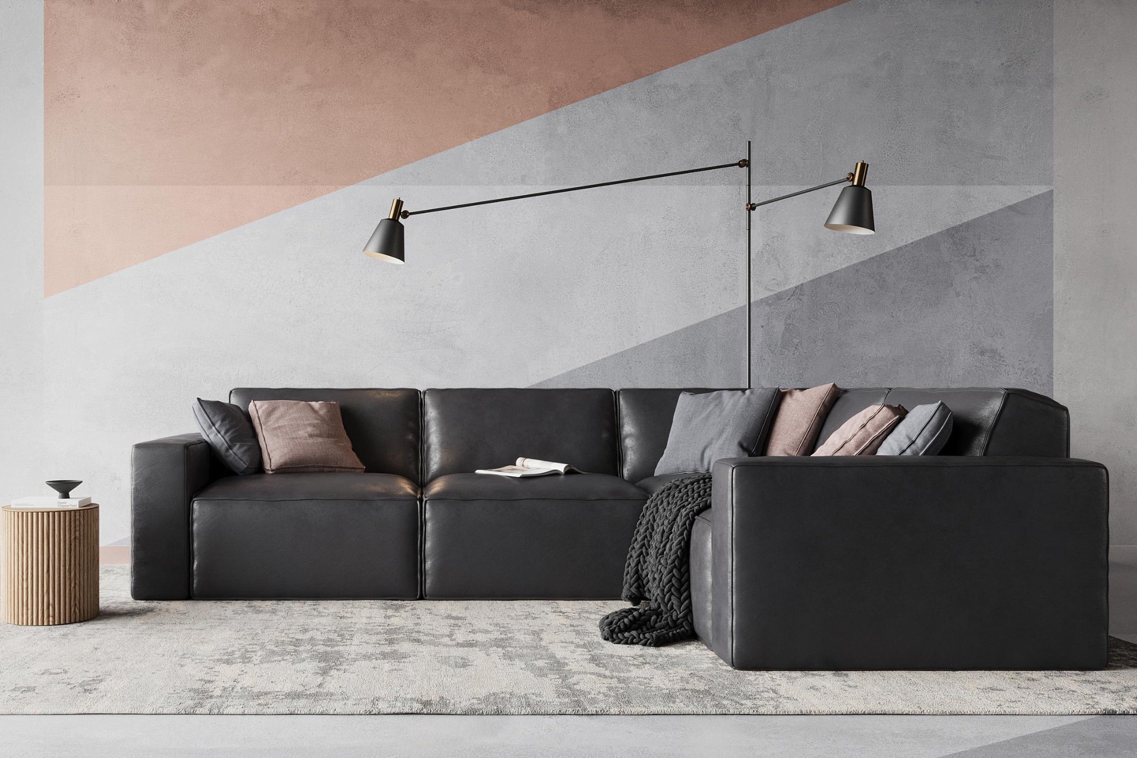 A modern living room with a dark leather sectional sofa, adorned with cushions and a black throw. A tall, dual-head floor lamp is positioned above. The wall features geometric patterns in neutral tones, and a small wooden side table is nearby.