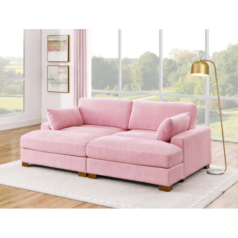 The spacious, light-filled living room showcases the Etta Avenue Mordecai 90'' Square Arm Sofa, elegantly positioned on a beige rug. A gold floor lamp stands beside this large, pink sectional sofa, while expansive windows offer views of trees and greenery outside.