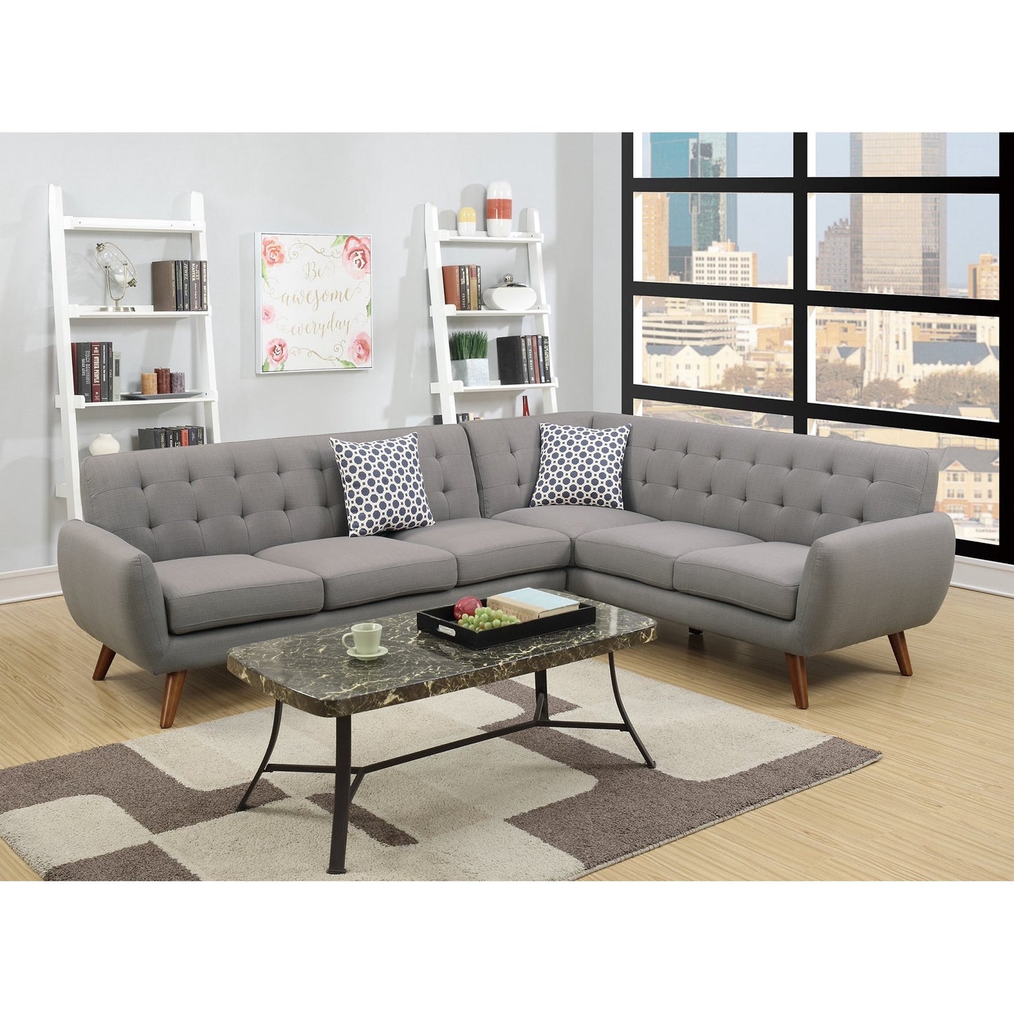 A contemporary living room featuring a Retro Modern Grey Sectional Sofa in an L-shape, adorned with patterned cushions. It includes a marble coffee table and a geometric rug. Against the wall, there's a white shelving unit filled with books and decor, while a large window provides a view of the cityscape.