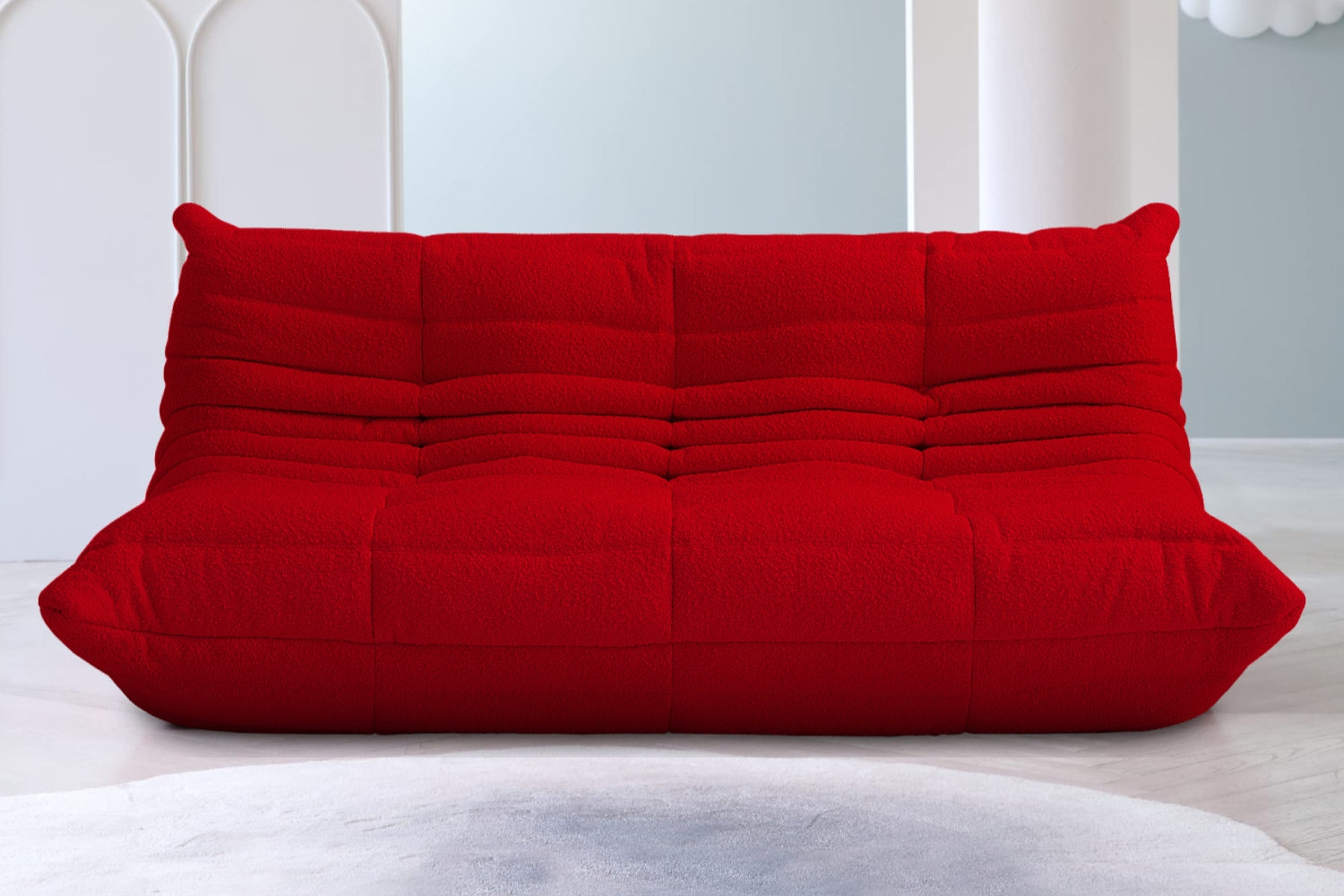 A vibrant red sofa with a plush, textured design and tufted details is placed in a modern room with light gray walls and abstract white wall decor in the background. The floor is covered with a gradient gray carpet.