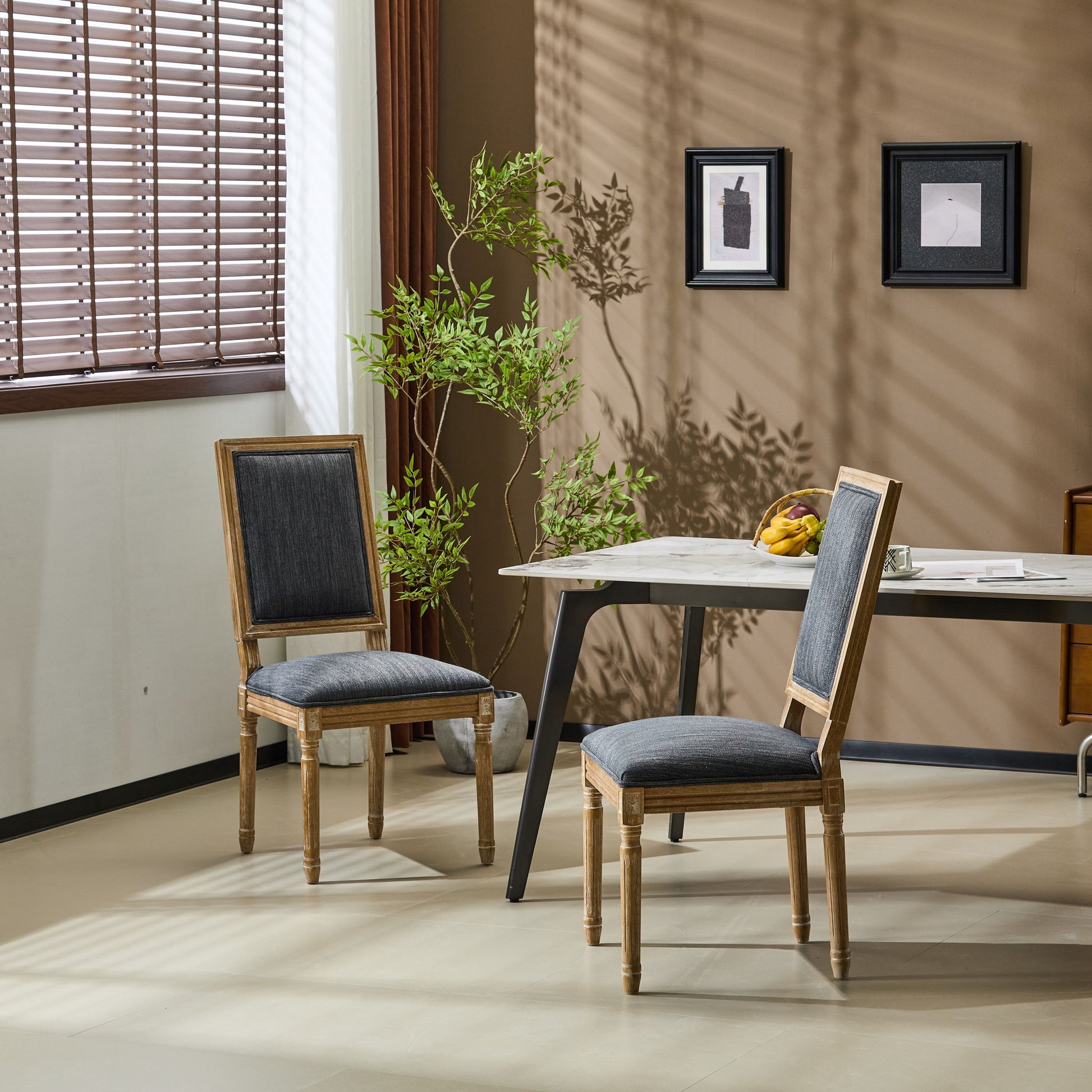 Two French Country Style Dining Chairs with upholstered seats and fluted legs sit by a modern table in a bright room with beige walls, a potted plant, framed art, and sunlight casting shadows through window blinds.