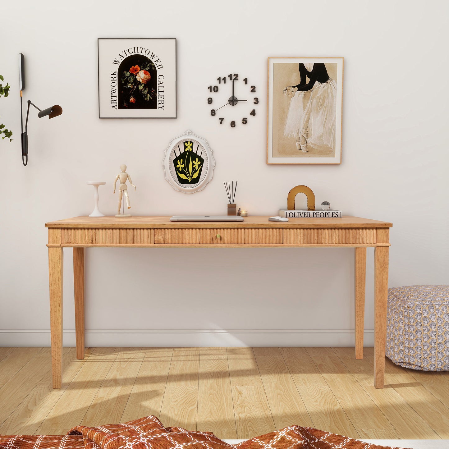 The Dumont - Modern Farmhouse 1 Drawer Fluted Home Office Writing Desk in Natural Blonde sits against a white wall with framed art, a black clock, and decor; a pouf and plaid blanket complete the cozy, minimalist setup.