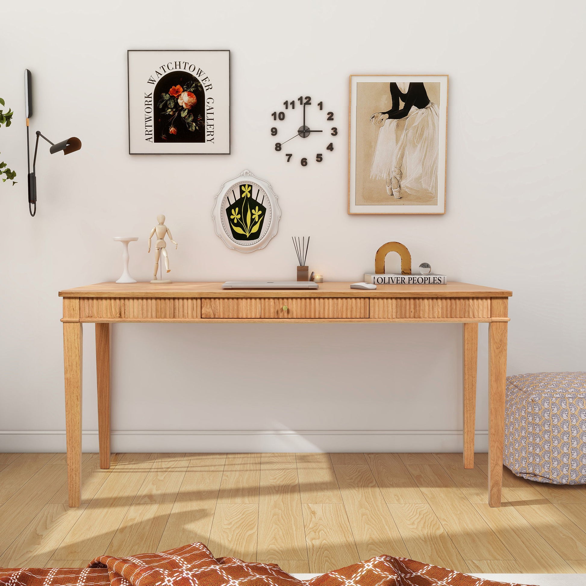 The Dumont - Modern Farmhouse 1 Drawer Fluted Home Office Writing Desk in Natural Blonde sits against a white wall with framed art, a black clock, and decor; a pouf and plaid blanket complete the cozy, minimalist setup.