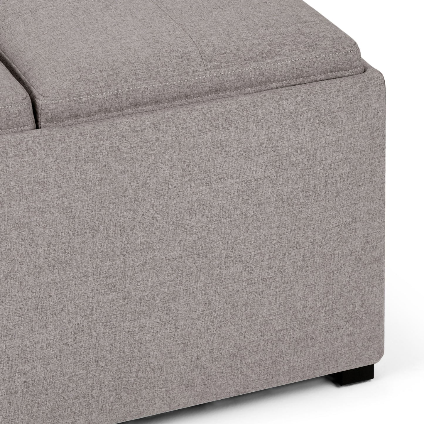 Close-up of the Avalon Square Coffee Table Storage Ottoman with light gray textured upholstery and black wooden legs, shown against a white background.