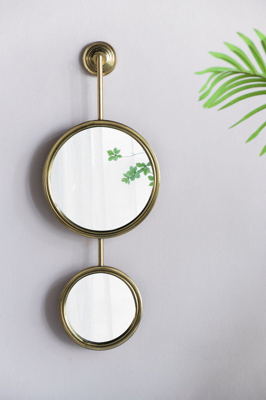 Two 2 Circle Mirrors For Wall Decor, Unique Contemporary Wall Mirror For Living Room Bedroom Entryway - Gold, are mounted vertically on a light-colored wall. Green plant leaves are reflected in the top mirror and partly visible on the right.