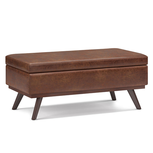 The Owen Lift Top Large Coffee Table Storage Ottoman features a brown rectangular design with angled wooden legs, mid-century style, a lift-top lid, and a smooth faux leather finish, shown against a white background.