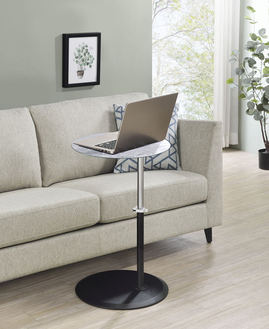 A modern living room features a light beige sofa with a geometric cushion, a laptop on the Orbit 15.5" End Table with Height Adjustable Marble Textured Top, a framed plant picture on the wall, and large windows filling the space with natural light.