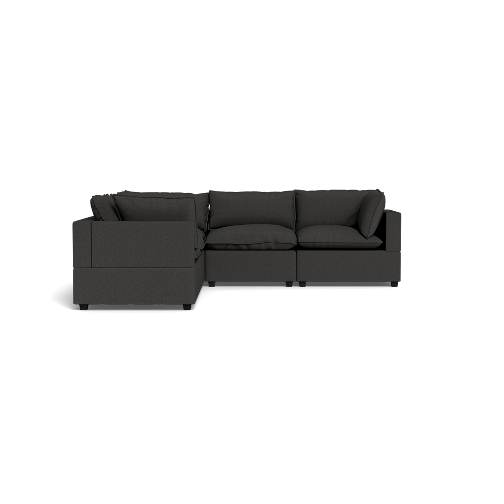 The Kova Pillow Cushion Corner Sectional is a modern, dark gray L-shaped sofa with cushions and armrests, set against a solid black background.