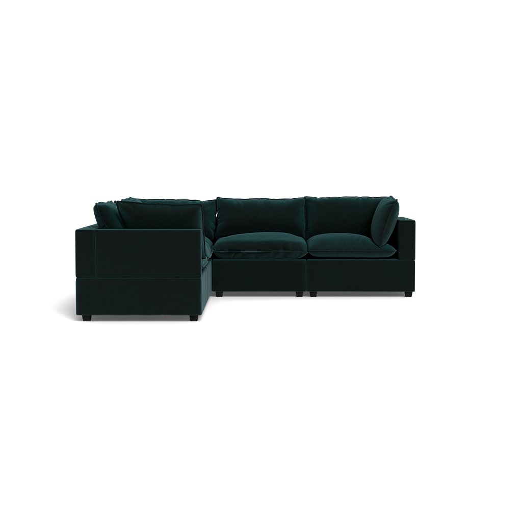 The Kova Pillow Cushion Corner Sectional, a dark green L-shaped sofa with plush cushions and wide armrests, is set against a solid black background.