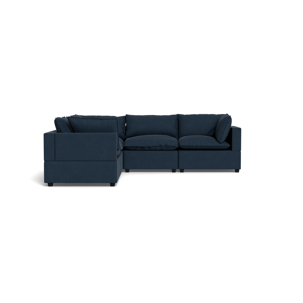 The Kova Pillow Cushion Corner Sectional is a dark blue L-shaped sofa with plush seat and back cushions, wide armrests, and a modern minimalist design, shown against a black background.