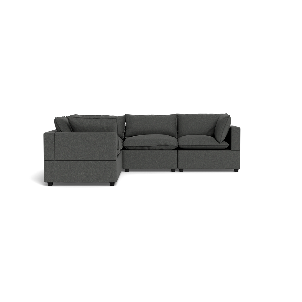 The Kova Pillow Cushion Corner Sectional is a modern dark gray L-shaped sofa with padded cushions and armrests, showcased against a plain black background.