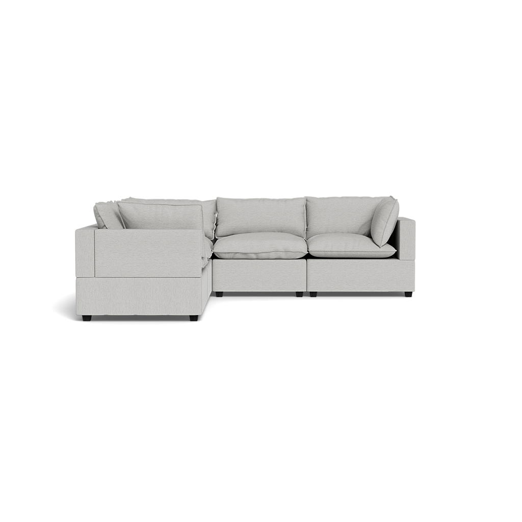 The Kova Pillow Cushion Corner Sectional, a light gray L-shaped sofa with wide armrests and plush cushions, is set against a plain black background.