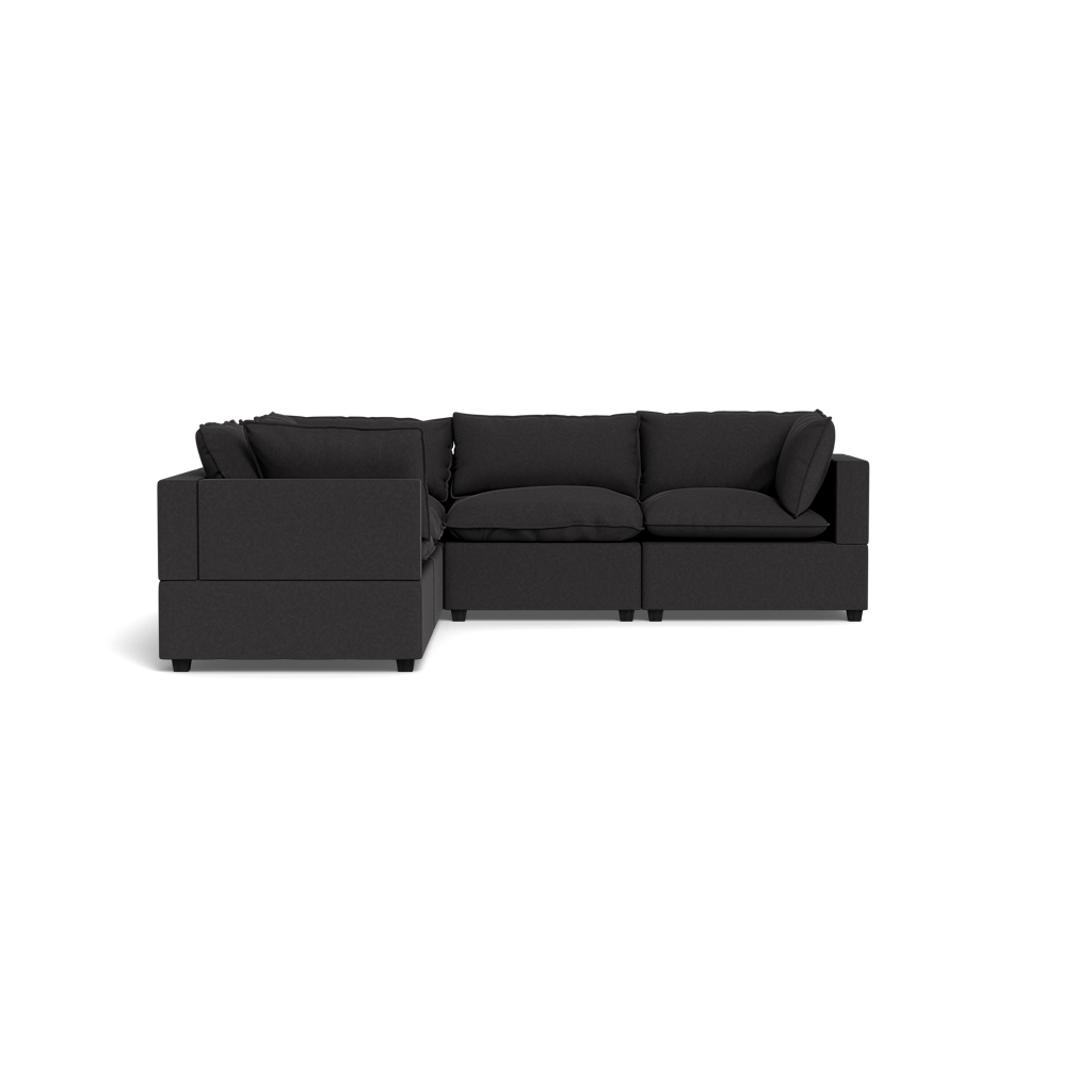 The Kova Pillow Cushion Corner Sectional is a modern, dark gray sofa with thick cushions and armrests, shown against a black background.