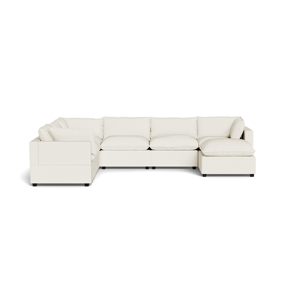 The Kova Pillow Cushion Grand Corner + Ottoman is an L-shaped sectional with plush cushions and a right-side chaise, upholstered in off-white fabric, set against a plain black background.