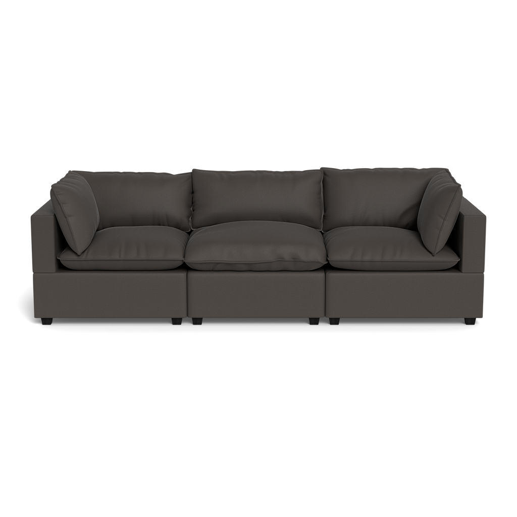 The Kova Pillow Cushion Sofa 122” is a modern, dark gray three-seater with wide armrests and loose back cushions, shown against a plain black background.