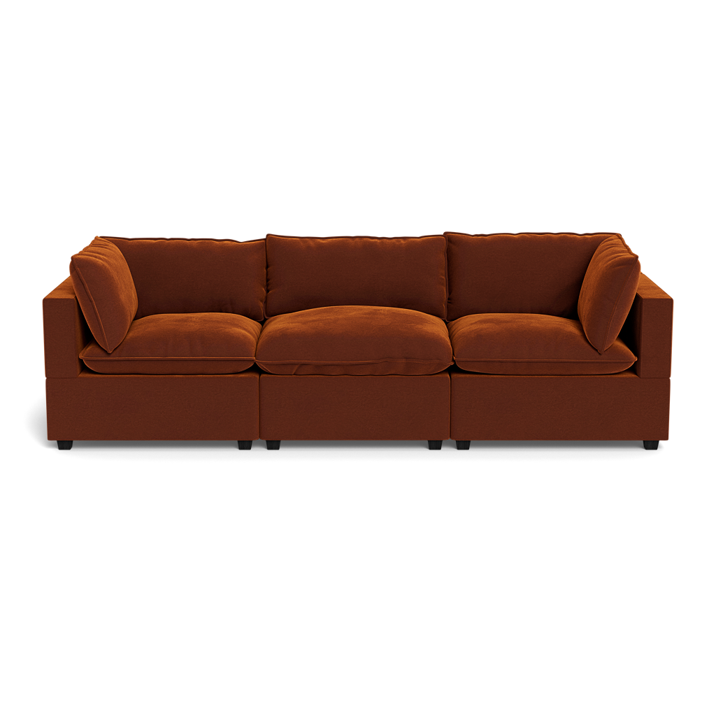The Kova Pillow Cushion Sofa 122" is a modern three-seater with rust-colored upholstery, square arms, and loose back and seat cushions, displayed against a plain black background.