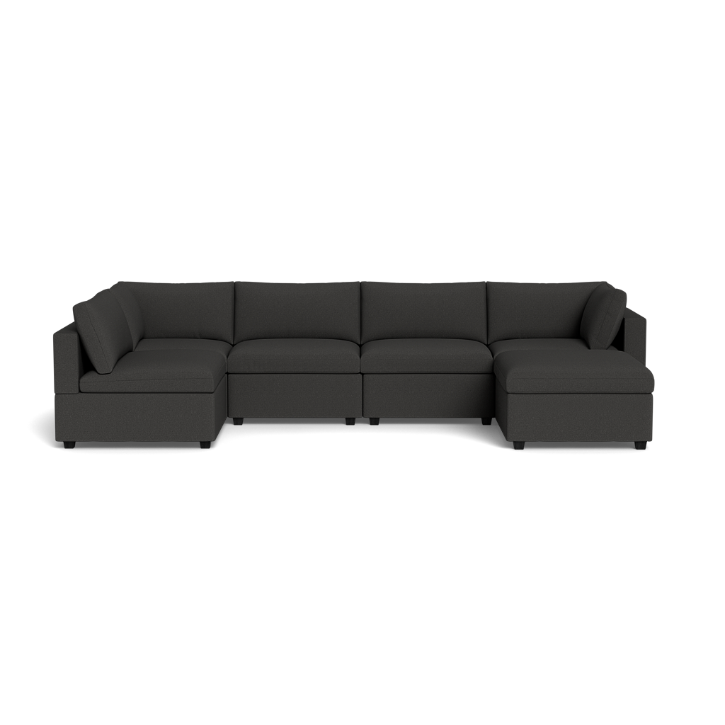 The Kova Box Cushion U-Shape is a modern, dark gray sectional sofa featuring three sections, low backrests, and square armrests, displayed against a plain black background.