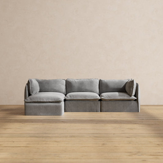 The Modular Performance 3-Seater Sectional in a modern light gray, featuring plush cushions, is placed against a neutral, textured wall. The wooden floor adds warmth to the minimalist room setting.