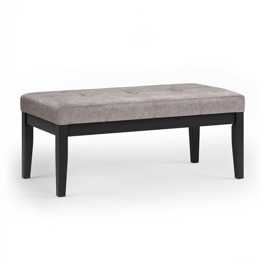 The Lacey Upholstered Tufted Ottoman Bench features a light gray cushioned, tufted seat and four black wooden legs, displayed on a white background.