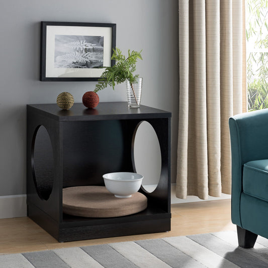 The Circle Design Comfortable Pet End Table With Removable Mat - Red Cocoa features circular cutouts, a round cushion inside, and pairs well with decorative spheres, green foliage in a vase, a framed photo, and a nearby teal chair.