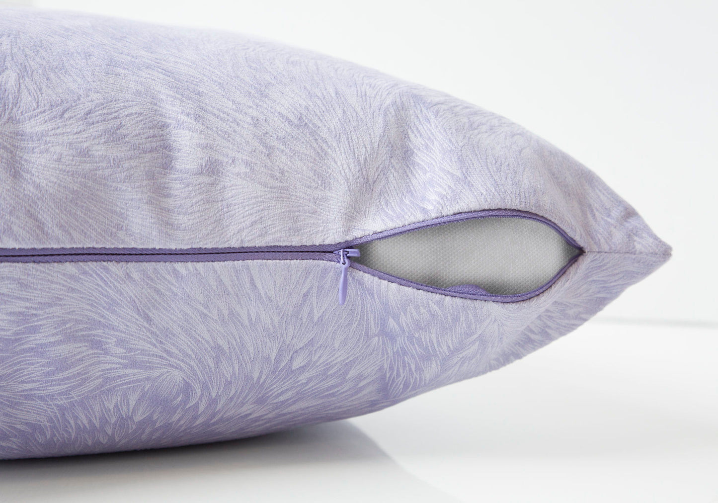 A close-up of the modern light purple Square Decorative Throw Pillow with insert included and hypoallergenic filling, showing a subtle textured pattern and a partially open zipper revealing the white inner material on a white surface.