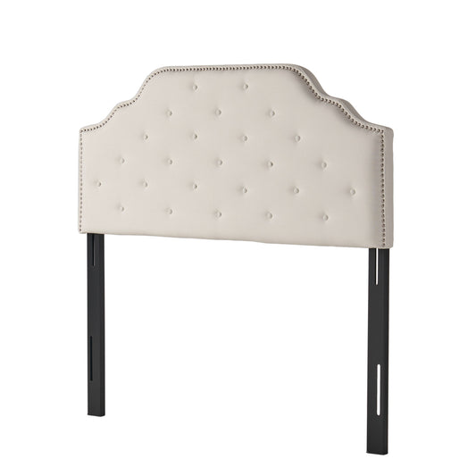 The Charismatic Size Headboard features beige upholstery, a scalloped top, button tufting, nailhead trim, and is supported by two black metal legs with adjustable slots.