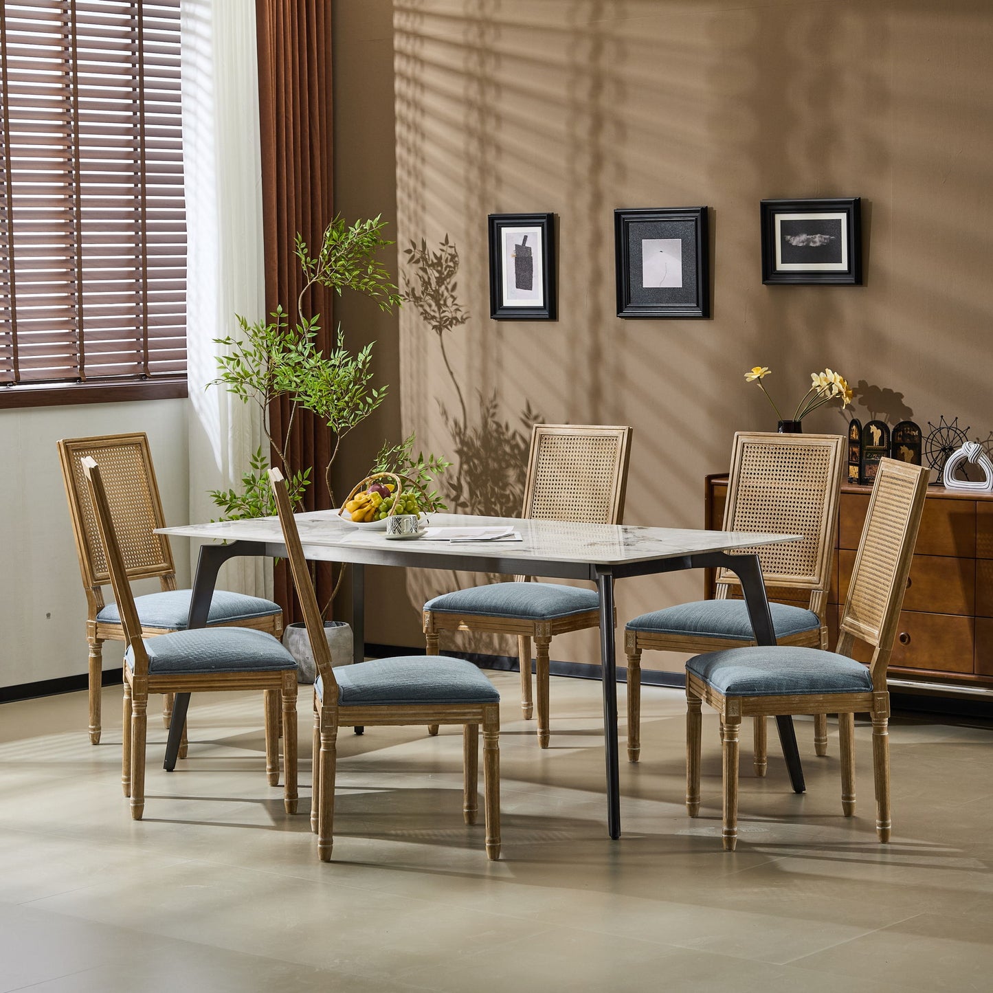 A modern dining room with a rectangular table, six French Country Dining Chairs featuring rectangular cane backs and smooth upholstered seats, a plant centerpiece, wall art, and natural light from window blinds.
