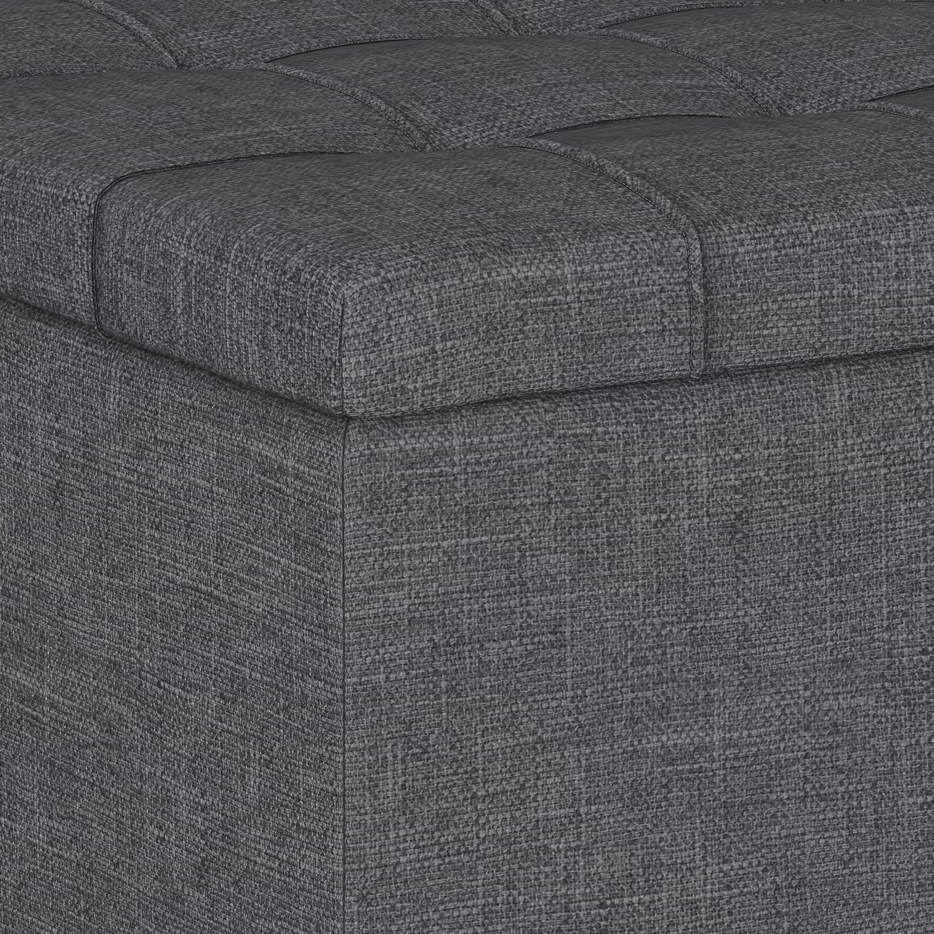 Close-up of the corner of the Harrison Upholstered Coffee Table Storage Ottoman, featuring dark gray textured fabric and a tufted, cushioned top.