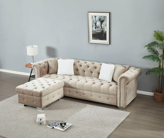 A modern living room features the 4 Seater Oversized L Shaped Reversible Sectional Sofa in beige with white pillows and a matching ottoman, set on a light rug alongside grey walls, a floor lamp, framed wall art, side table, and potted plant.