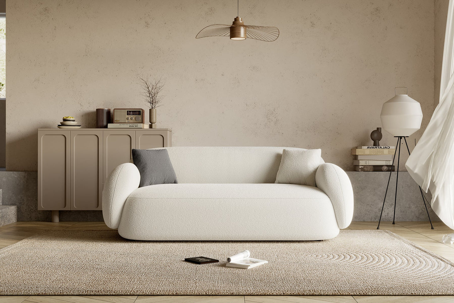 A cozy living room features the Dori Sofa by Acanva, complemented by two cushions. Behind it stands a wooden cabinet adorned with decor items and a vintage radio. A woven rug covers the floor, with a phone and a book resting on it. Overhead, a pendant light illuminates the space.