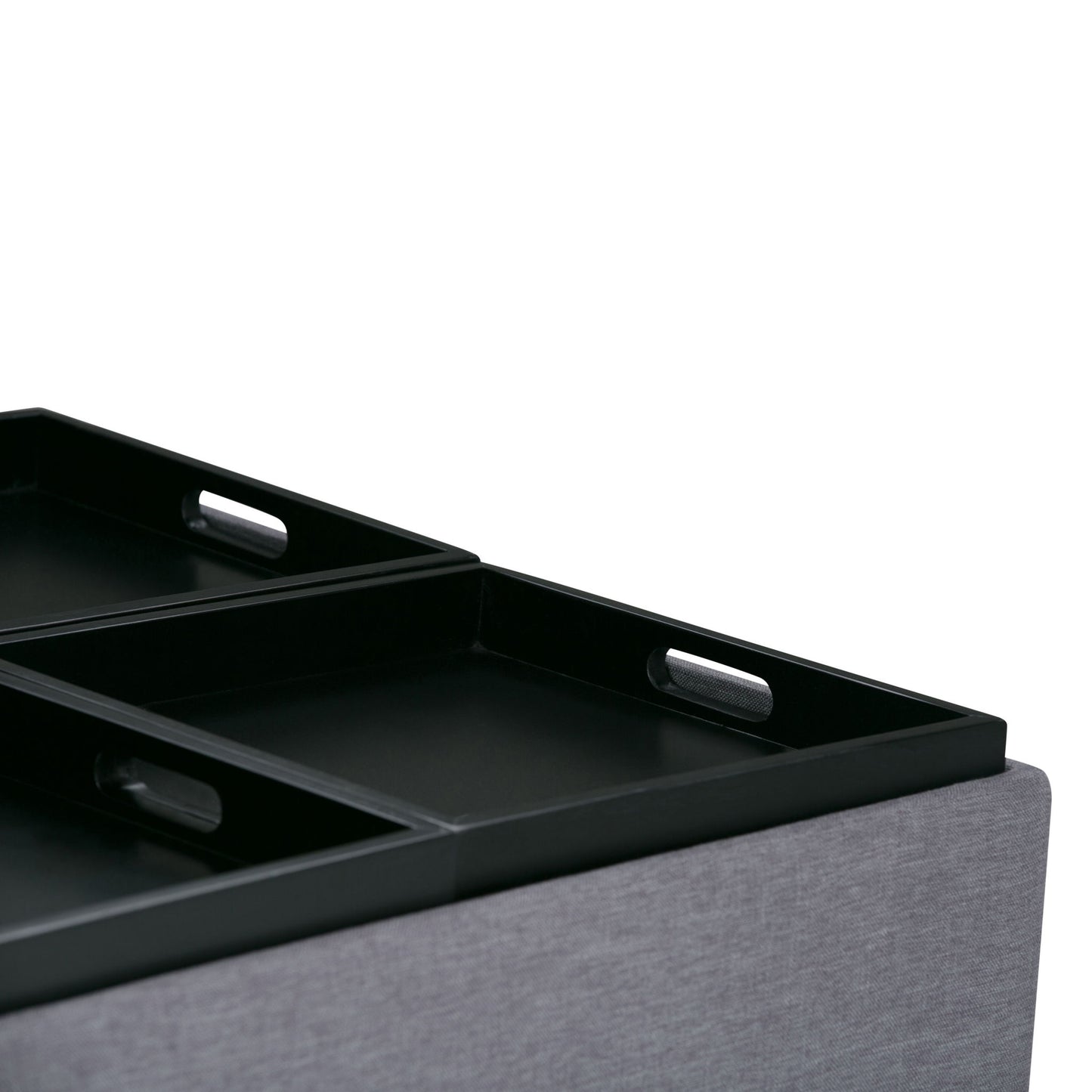Close-up of the Avalon Square Coffee Table Storage Ottoman, featuring black rectangular trays with handles, placed on a light gray upholstered surface against a white background.