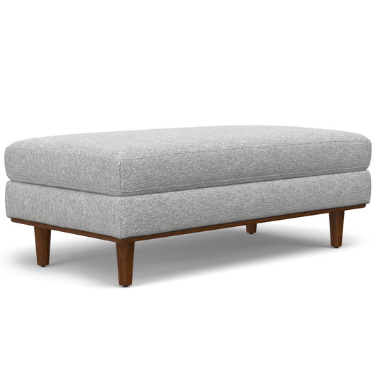 The Morrison - Handcrafted Ottoman is a rectangular, light gray upholstered piece with short, angled wooden legs in a mid-century modern style.
