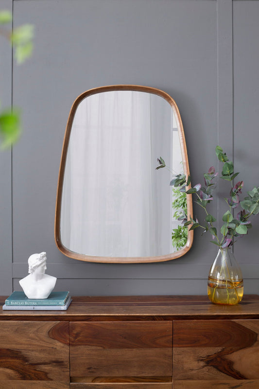 A wooden dresser holds a white bust, two stacked books, and a glass vase with foliage. Above, the Irrgeular Mirror With Wood Frame, Wall Mirror For Living Room Bathroom Entryway - Brown hangs on a gray paneled wall.