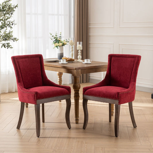 Two Ultra Side Dining Chairs with thickened fabric and neutrally toned solid wood legs, bronze nail head trim, surround a small wooden table set with two teacups, a candle, and flowers in a bright room with light floors and large windows.