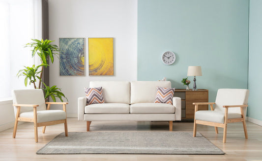 A modern living room features the Bahamas - Sofa Set With 2 Throw Pillows, two armchairs, a colorful rug, side table with lamp, wall art, a clock, and a tall plant by the window. The wall is partly white and partly light blue.