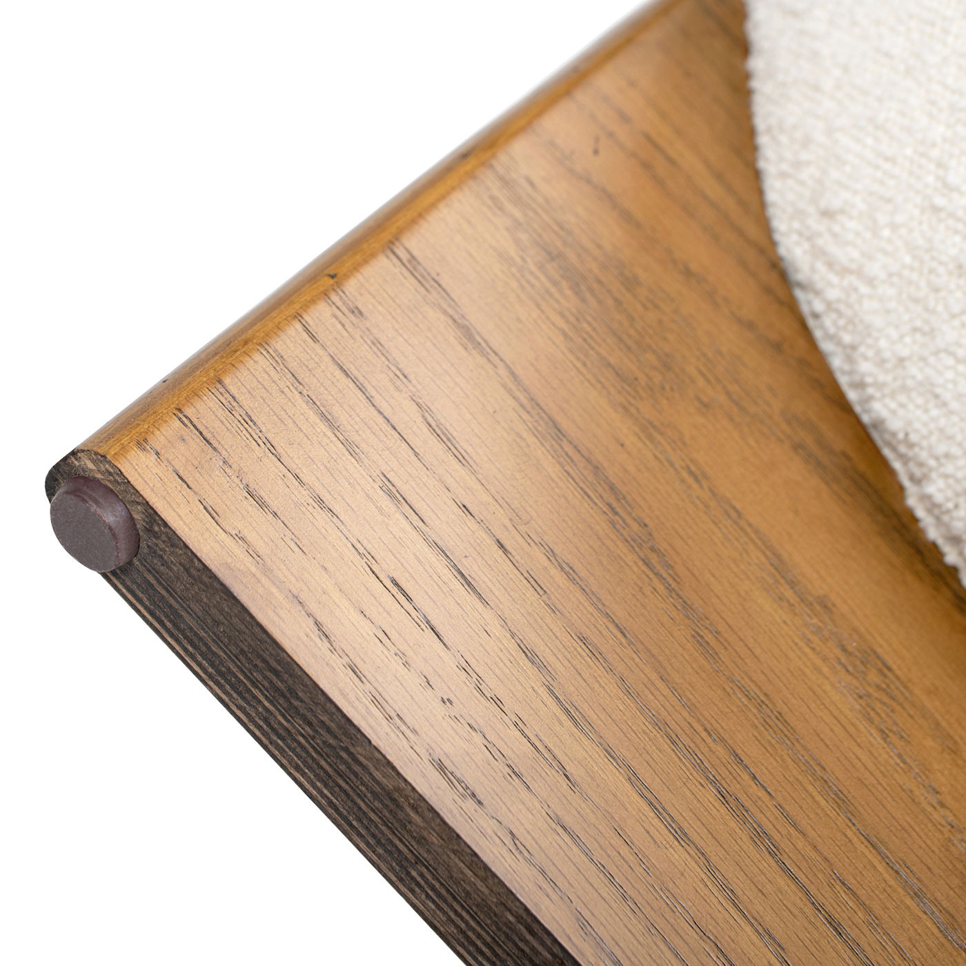 Close-up of the Bali - Round Upholstered Ottoman's wooden base, showcasing its smooth finish, rounded edge with a brown rubber cap, and partially visible textured cream-colored upholstery on the right.