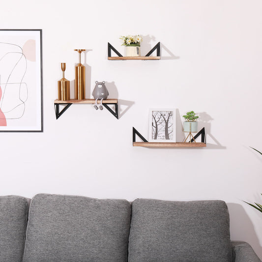 Three Floating Shelves, Long Wall Shelves (Set of 3) in natural wood with black brackets display gold vases, a gray bear figurine, framed art, flowers, and a potted plant above a gray sofa. A modern abstract print hangs on the left wall.