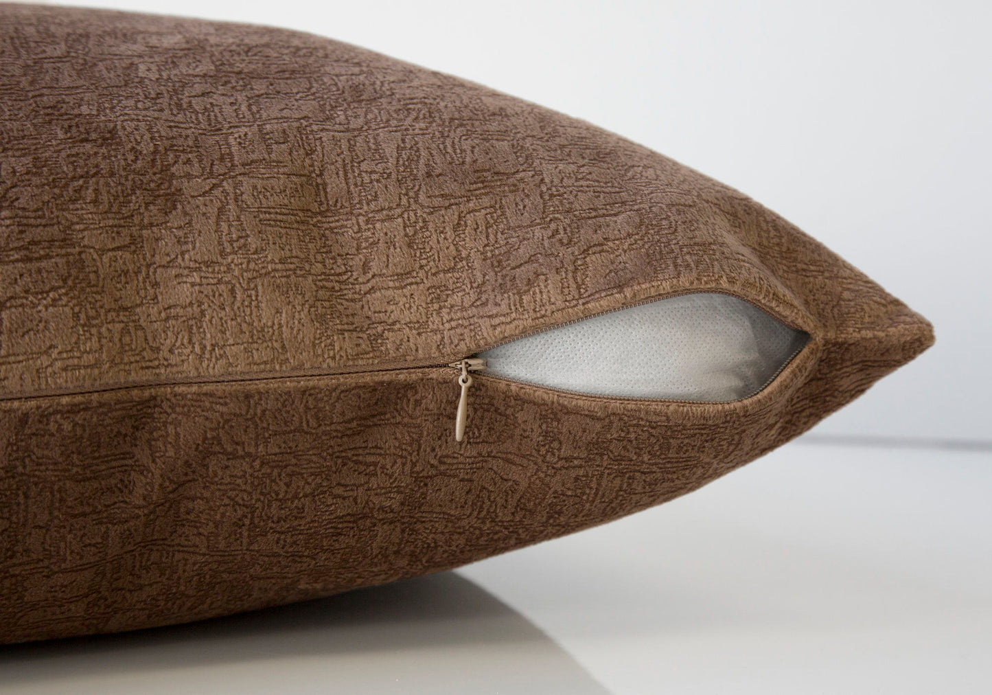 A close-up of a modern, brown decorative throw pillow with a partially open zipper exposing the hypoallergenic white insert. The square pillow sits on a smooth, reflective surface. Insert included.