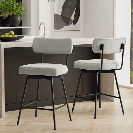Two Giselle Swivel Counter Height Stools, featuring light gray cushioned seats and backs with black metal legs, are set in a modern kitchen with a dark island, marble countertop, and abstract wall art. Set includes 2 stools.