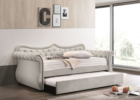 A modern bedroom featuring the Adkins Twin Daybed With Trundle in beige, styled with striped bedding and framed art. Large windows fill the space with natural light and a violin rests on the bed, overlooking a garden view.