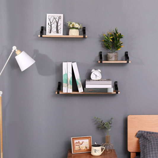 A set of 3 natural wood Floating Shelves is wall-mounted above a nightstand and bed, displaying books, a clock, photos, plants, and decor beside a white floor lamp in the bedroom.