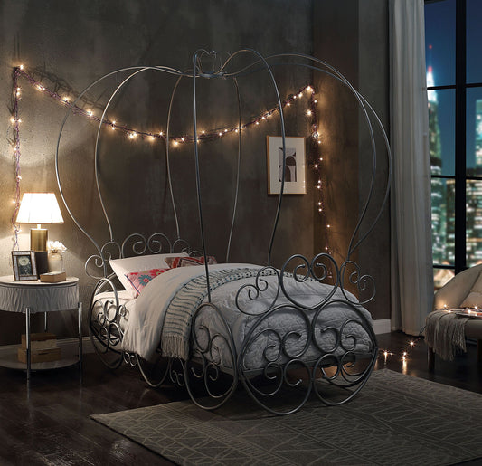A whimsical bedroom features the Priya Twin Bed With Canopy in silver, boasting delicate metal scrollwork, soft bedding, string lights on gray walls, and a large window revealing a nighttime cityscape.