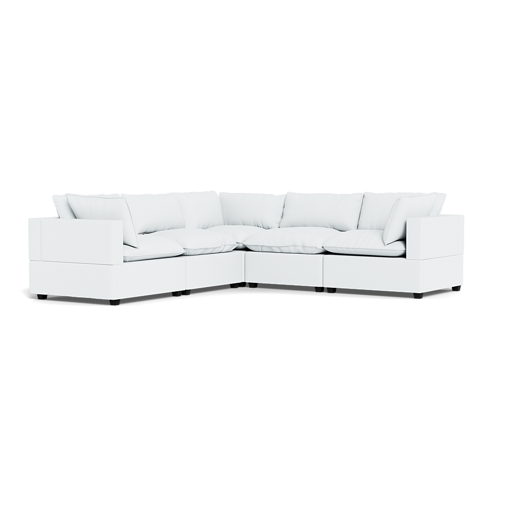 The Kova Pillow Cushion Corner Sectional features a modern white design with plush seat and back cushions, low-profile arms, and a right-angle corner silhouette, showcased against a plain black background.