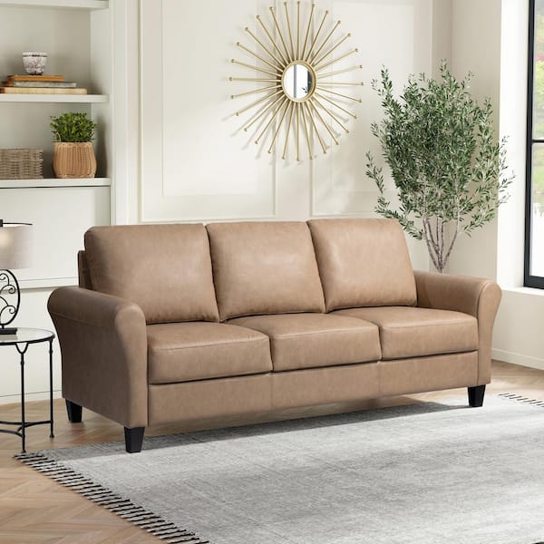 A dark grey Wesley 3-seater sofa with round arms is placed on a light gray rug in a modern living room, with a sunburst mirror, decor shelves, a large potted plant, and a window letting in natural light behind it.
