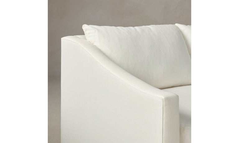 Close-up of The Sullivan 60" Sofa in Performance Linen Weave, featuring a white modern design with smooth fabric and an angled armrest. The backdrop is a soft beige, accentuating the cushion on the sofa.