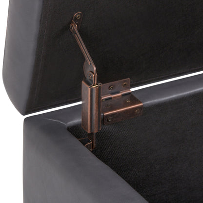 Close-up view of the Hamilton - Upholstered Storage Ottoman in a dark color, shown with its lid open to reveal the metal hinge mechanism attached inside for support.