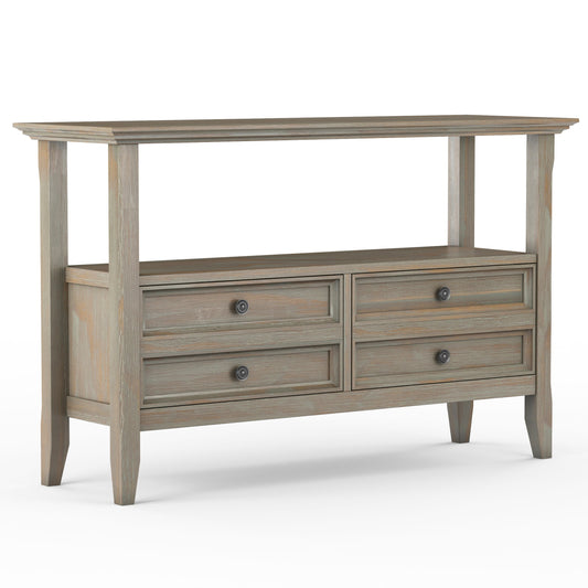 The Amherst Console Sofa Table is handcrafted from wood with a weathered gray finish, featuring an open top shelf, four drawers with round metal knobs, and stands on four tapered legs.
