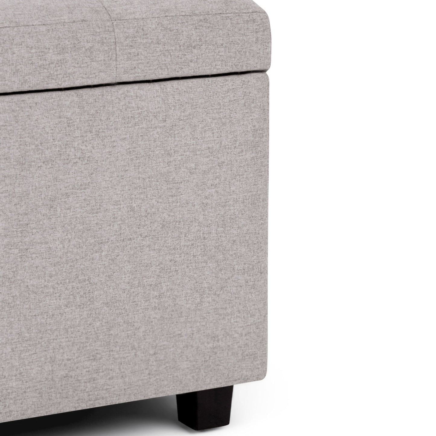 Close-up of the Cosmopolitan - Upholstered Storage Ottoman in light gray, featuring dark wooden legs. Shown against a white background, only part of the lid and two sides are visible.